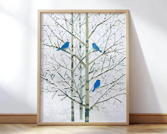 Minimalist watercolor-style art print featuring three bright bluebirds perched on slender, leafless tree branches. The trees have pale green and gray trunks with fine, angular twigs set against a soft white background, evoking a calm winter atmosphere. The artwork is framed in light wood and displayed leaning against a white wall on a hardwood floor.