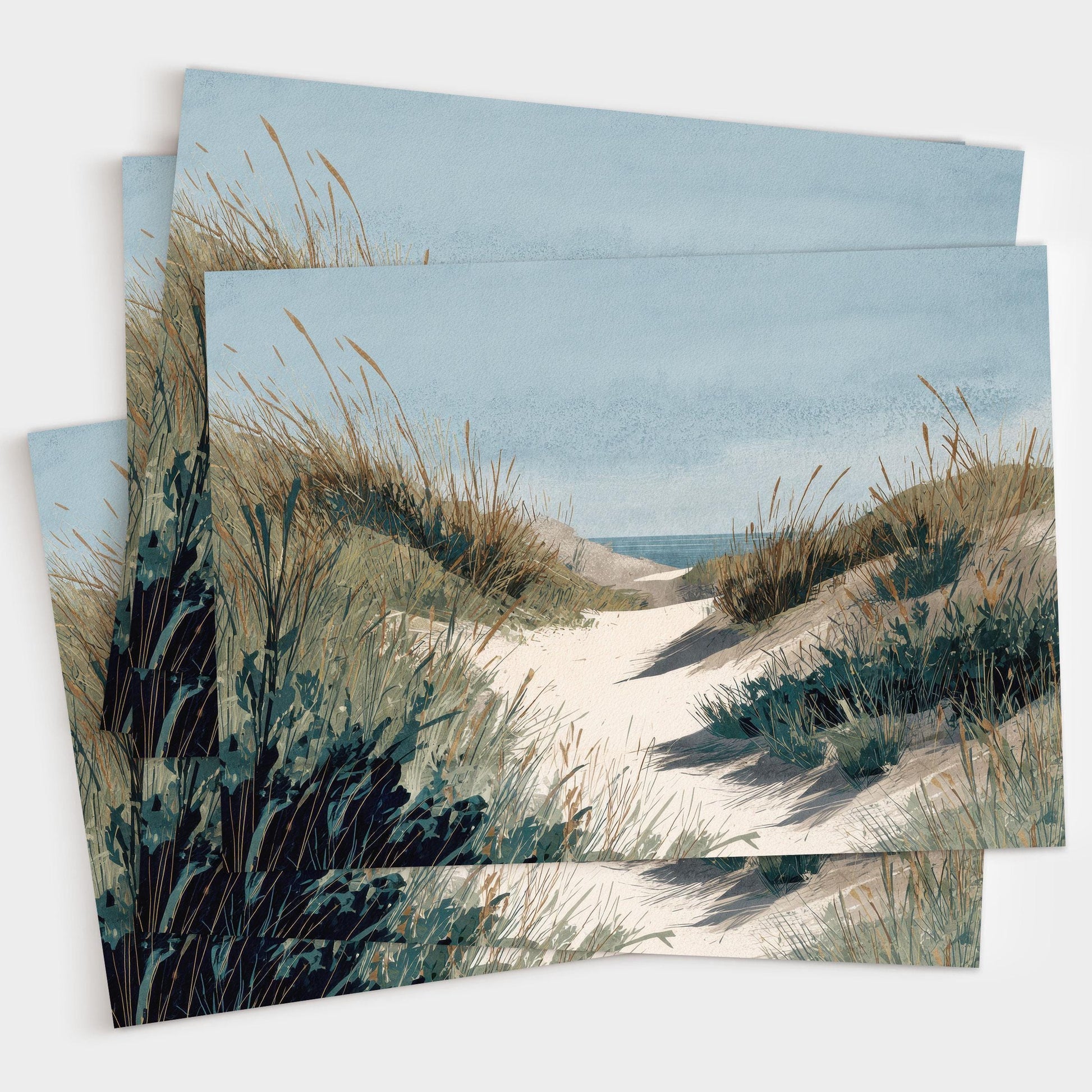 Set of greeting cards featuring a watercolor illustration of a sandy path through grassy dunes leading to the ocean under a calm blue sky, shown stacked in a small pile.