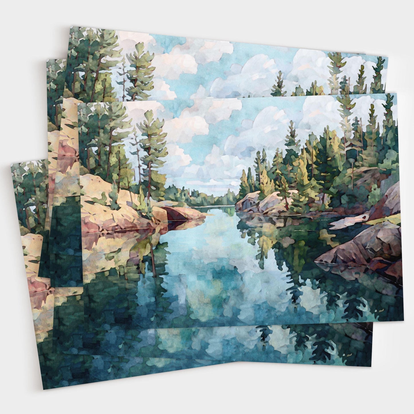 Set of greeting cards featuring a watercolor-style painting of a calm lake with rocky shores and pine trees, reflecting the cloudy sky and forest in the still blue water. Cards are fanned out in a layered display.