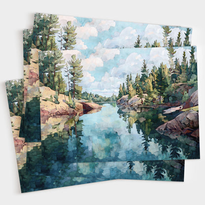 Set of greeting cards featuring a watercolor-style painting of a calm lake with rocky shores and pine trees, reflecting the cloudy sky and forest in the still blue water. Cards are fanned out in a layered display.