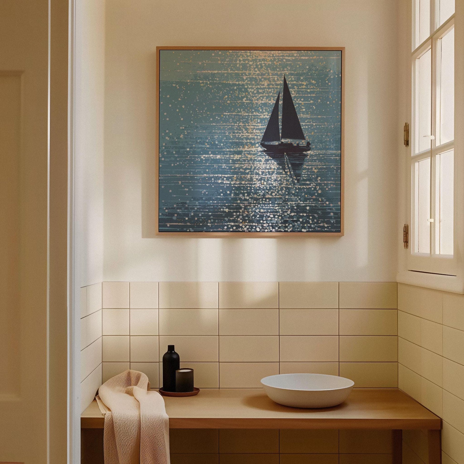 Framed sailboat print displayed in a serene, sunlit bathroom with warm neutral tones. The artwork shows a dark sailboat on sparkling blue water, with sunlight rendered in abstract, shimmering dots. Mounted above a minimalist wood vanity with a round vessel sink and matte black accessories, the piece adds a tranquil, coastal touch to the clean, modern space.