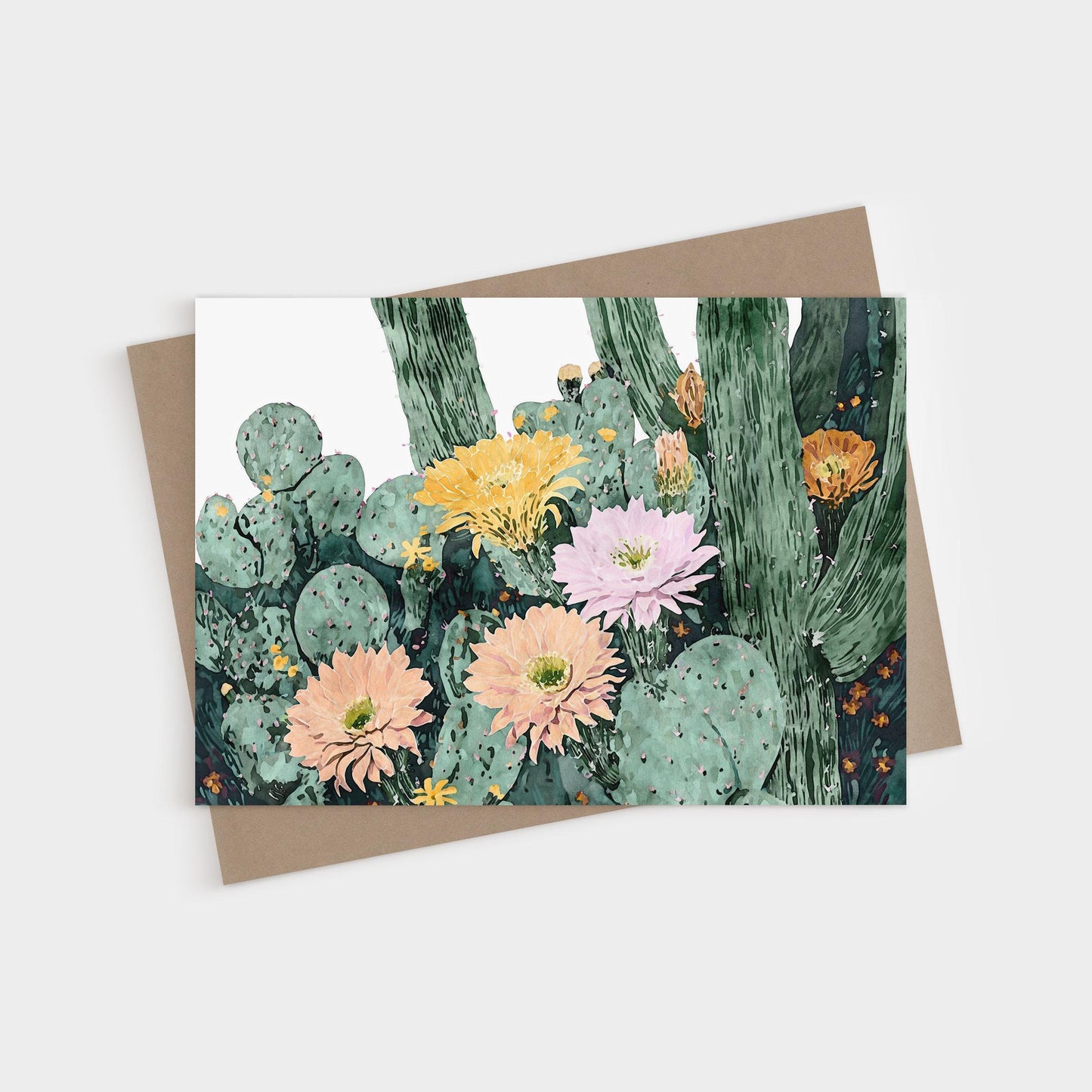 Greeting card featuring a watercolor illustration of blooming cacti with large flowers in soft peach, pink, yellow, and orange tones against green cactus pads and tall stems, paired with a natural brown envelope.