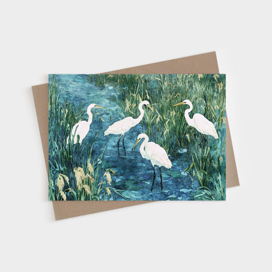 Greeting card featuring a watercolor-style painting of five white egrets standing in a marshy blue-green wetland, surrounded by tall grasses and reeds. Card is paired with a kraft envelope.