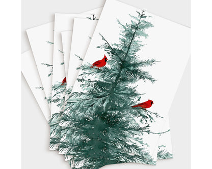 Set of greeting cards featuring a watercolor illustration of a pine tree with two bright red cardinals perched on its branches, fanned out to display multiple copies on a white background.