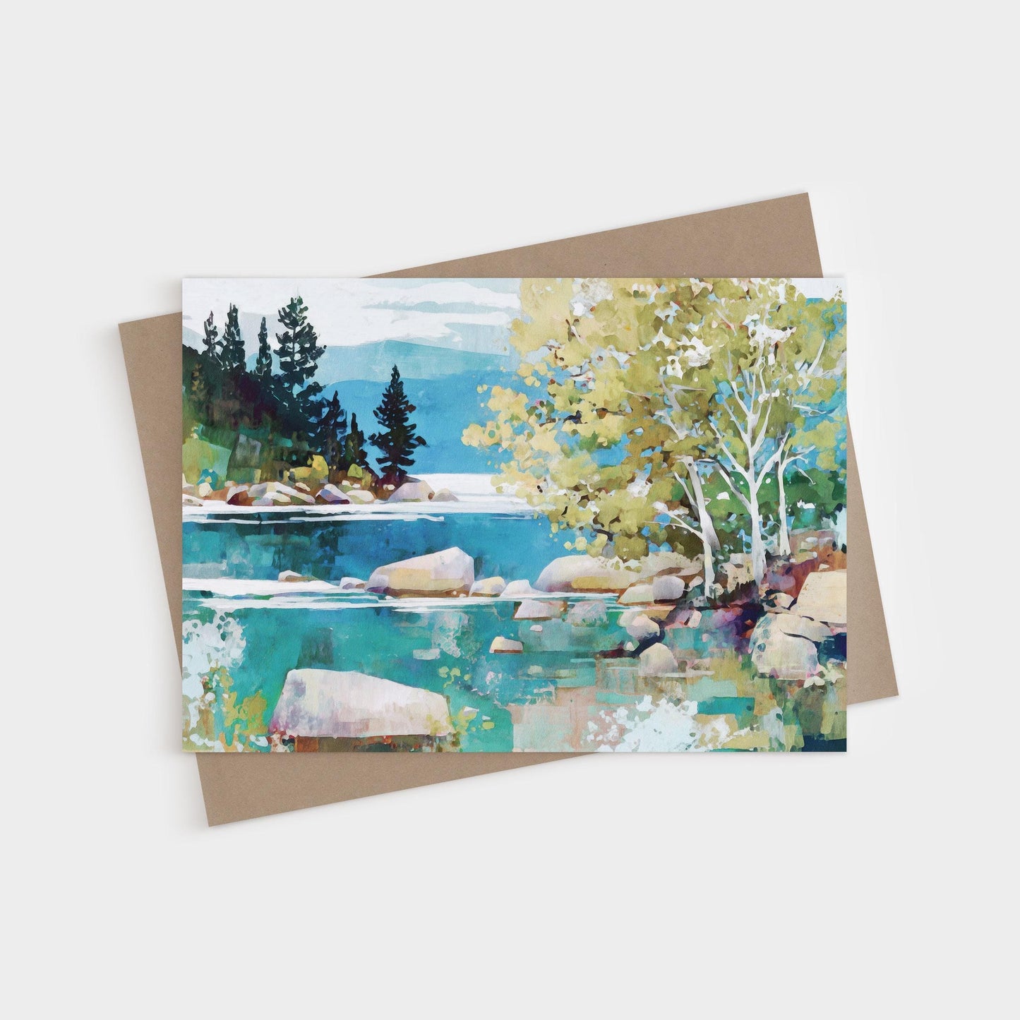 Greeting card featuring a modern impressionist landscape painting of a tranquil lake with turquoise water, smooth boulders, and shoreline trees. Birch trees with pale trunks and golden-green leaves stand in the foreground, while dark evergreens rise against distant mountains and a soft blue sky. Card is paired with a brown kraft envelope.