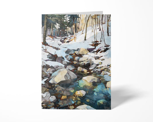 Greeting card standing upright, featuring a watercolor-style winter landscape of a rocky creek surrounded by snow and bare trees, with icy blue and green reflections in the water.