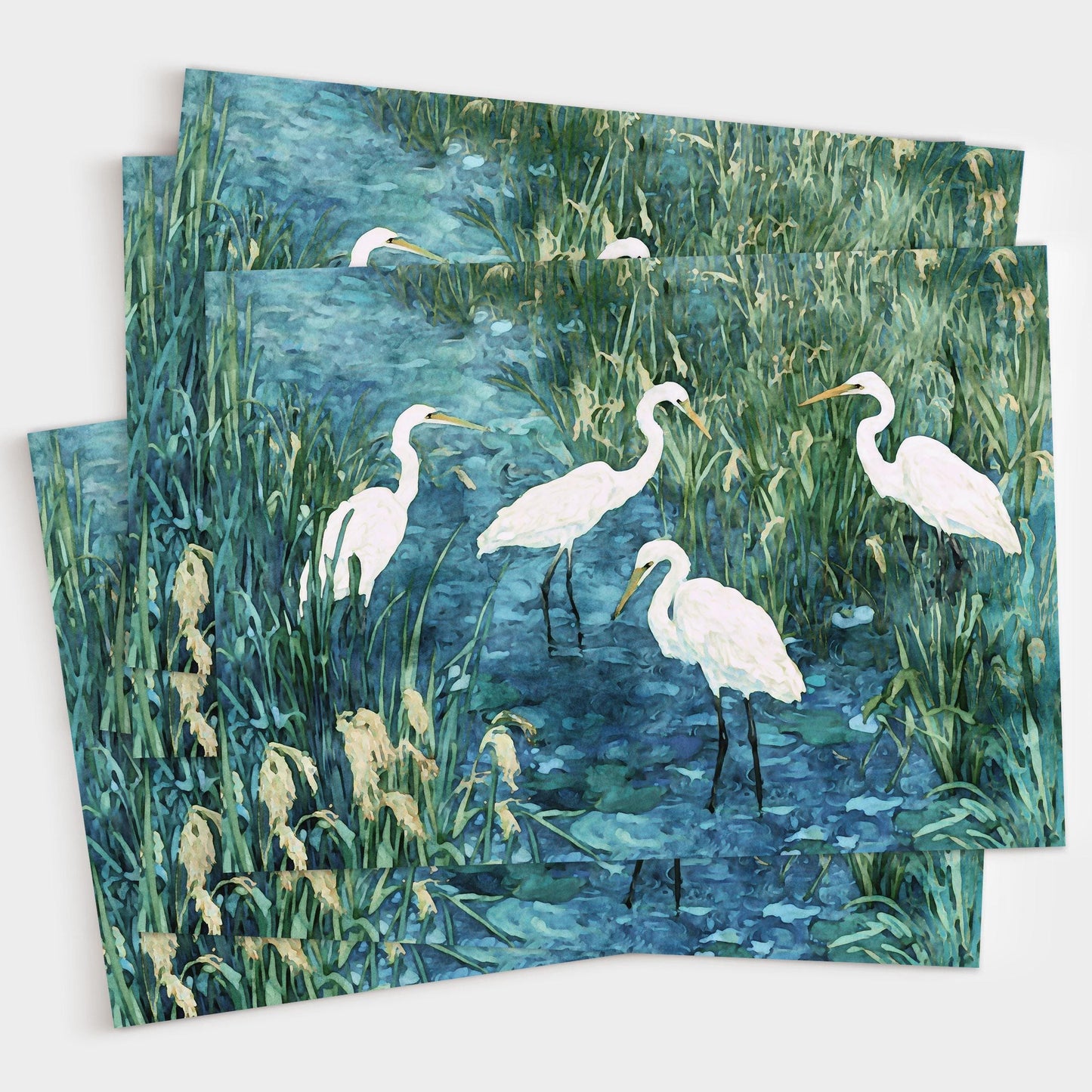 Set of greeting cards featuring a watercolor-style painting of five white egrets standing in a marsh with tall green grasses and deep blue water. Cards are fanned out in a layered display.