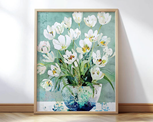 Framed art print of a watercolor-style bouquet of white tulips in a textured blue-green vase, set against a soft teal background. The painting combines loose brushwork and layered transparency for a modern botanical look, displayed in a light wood frame leaning against a wall on a hardwood floor.