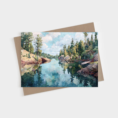 Horizontal greeting card featuring a watercolor-style painting of a calm northern lake, surrounded by rocky shores and evergreen pine trees, with reflections of the sky and clouds mirrored in the clear water.