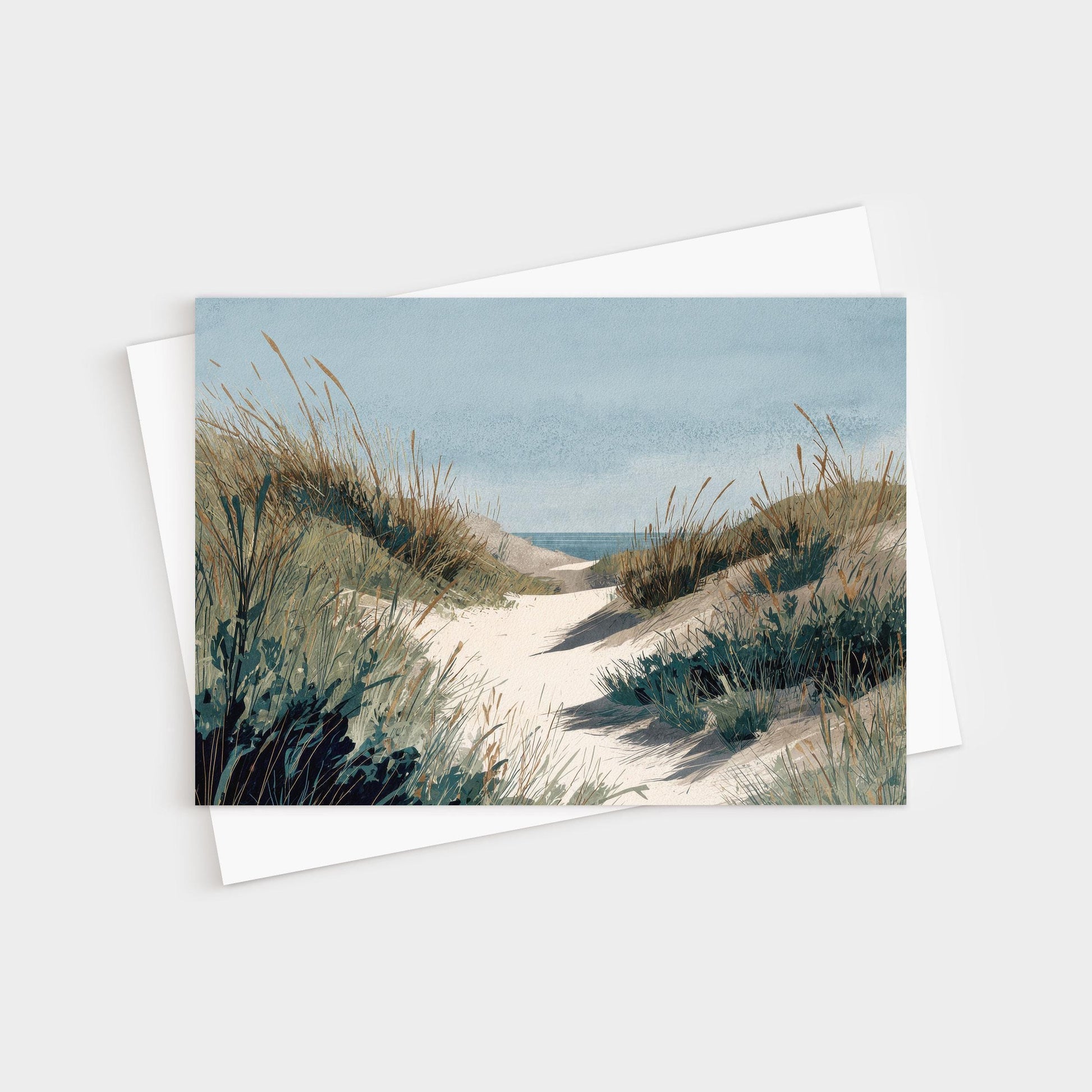 Greeting card featuring a serene watercolor illustration of a sandy path winding through grassy dunes toward the ocean, under a soft blue sky. A white envelope is placed behind the card.