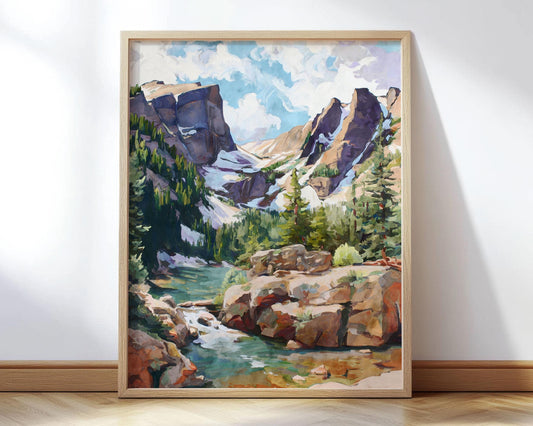 Framed landscape painting of a mountain scene with rocky peaks, pine forests, and a turquoise river winding through the foreground. Snow patches glisten on the cliffs under a partly cloudy sky. The artwork, rendered in a modern impressionist style with bold brushstrokes and rich earthy tones, leans against a white wall on a light wood floor, framed in a natural oak frame.