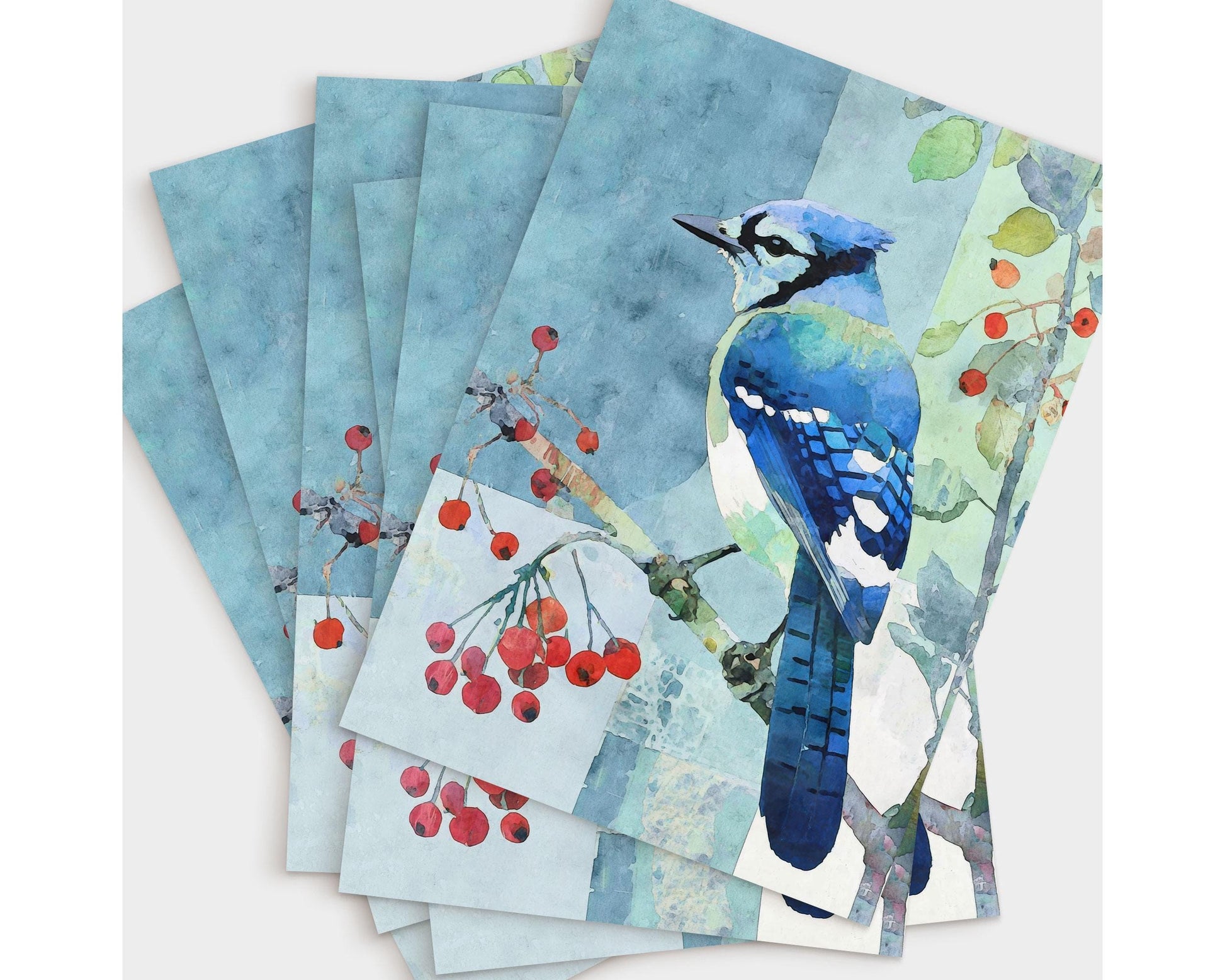 Set of greeting cards featuring a watercolor blue jay perched on a branch with red berries, surrounded by abstract blue and green tones. The cards are fanned out in a stack, showcasing the detailed bird illustration and soft, painterly background.