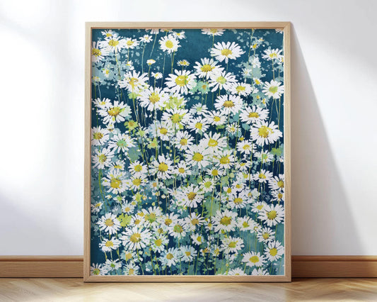 Framed art print featuring a dense field of white daisies with yellow centers against a deep teal-blue background, rendered in a loose, painterly watercolor style. The wooden frame rests on a light wood floor, leaning against a white wall in soft natural light.