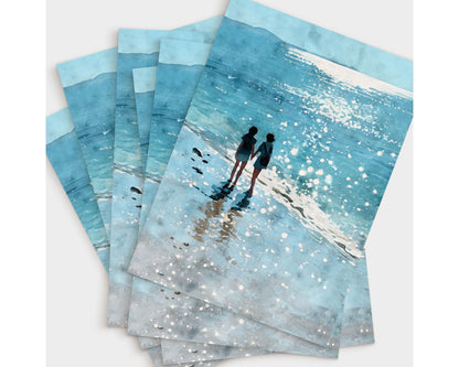 Set of five greeting cards fanned out, each featuring a watercolor-style illustration of two people holding hands at the edge of a shimmering ocean, with sparkling reflections and soft blue tones.