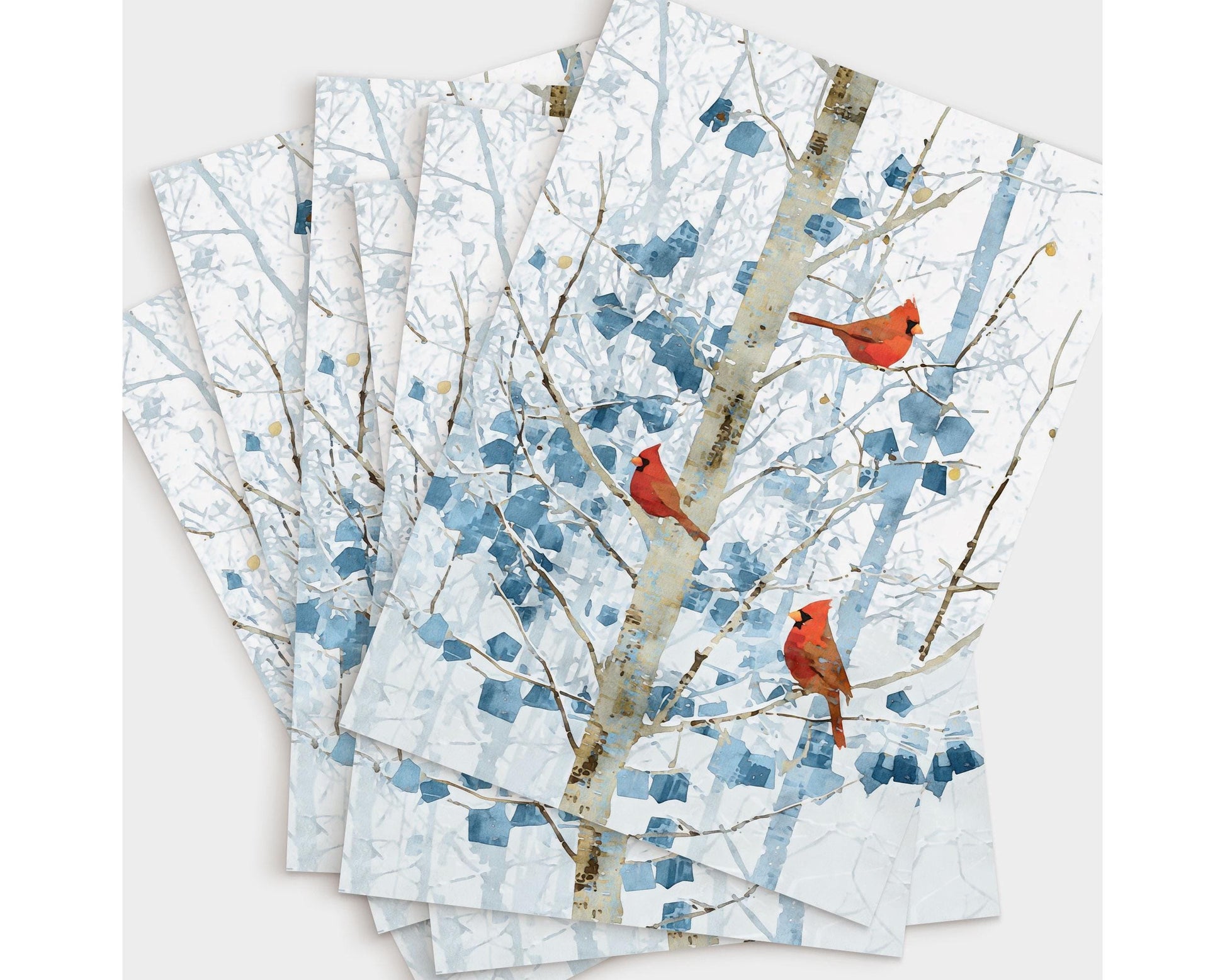 Set of winter-themed greeting cards fanned out on a light surface, each featuring three bright red cardinals perched on pale branches with abstract blue leaves. The repeated design creates a layered, overlapping display of the snowy forest artwork.