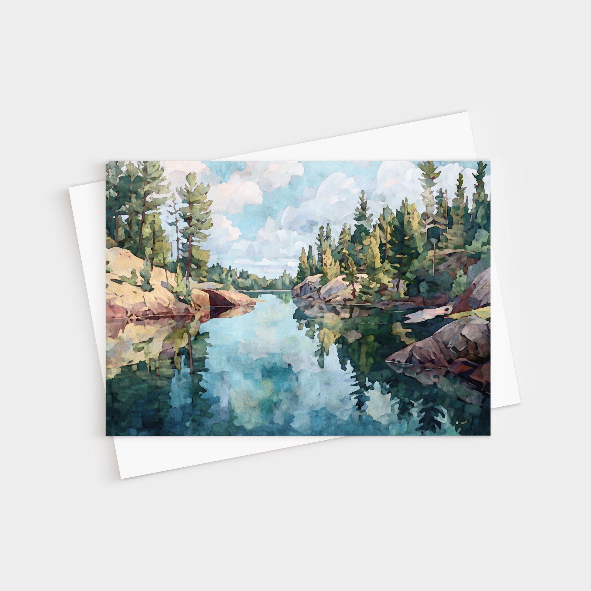 Horizontal greeting card featuring a watercolor-style painting of a calm northern lake, surrounded by rocky shores and evergreen pine trees, with reflections of the sky and clouds mirrored in the clear water.