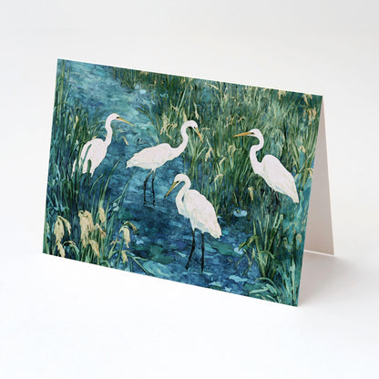 Folded greeting card featuring a watercolor-style painting of five white egrets wading in a marshy wetland, with tall green grasses and blue water. Displayed upright against a plain white background.