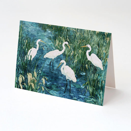 Folded greeting card featuring a watercolor-style painting of five white egrets wading in a marshy wetland, with tall green grasses and blue water. Displayed upright against a plain white background.