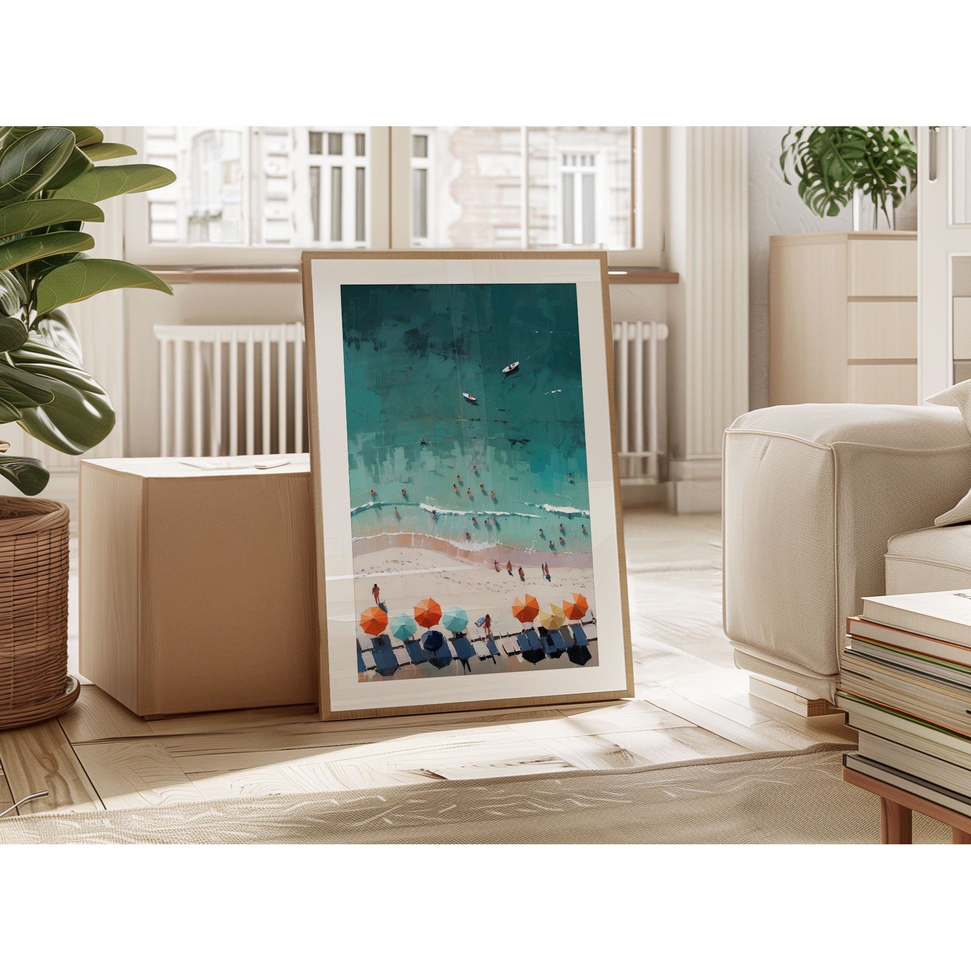 Framed abstract aerial beach artwork leaning against a wall in a modern living room with a plant, box, and books nearby.