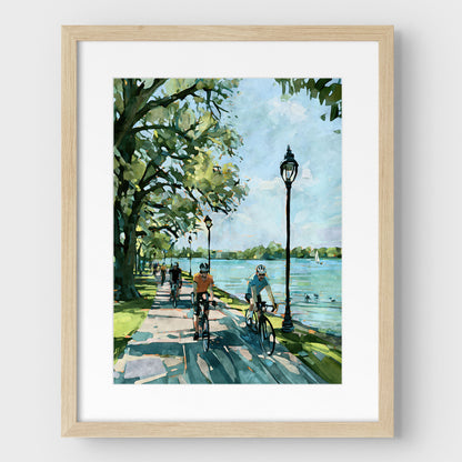 Matted Minneapolis Chain of Lakes cyclist art print in a natural wood frame.