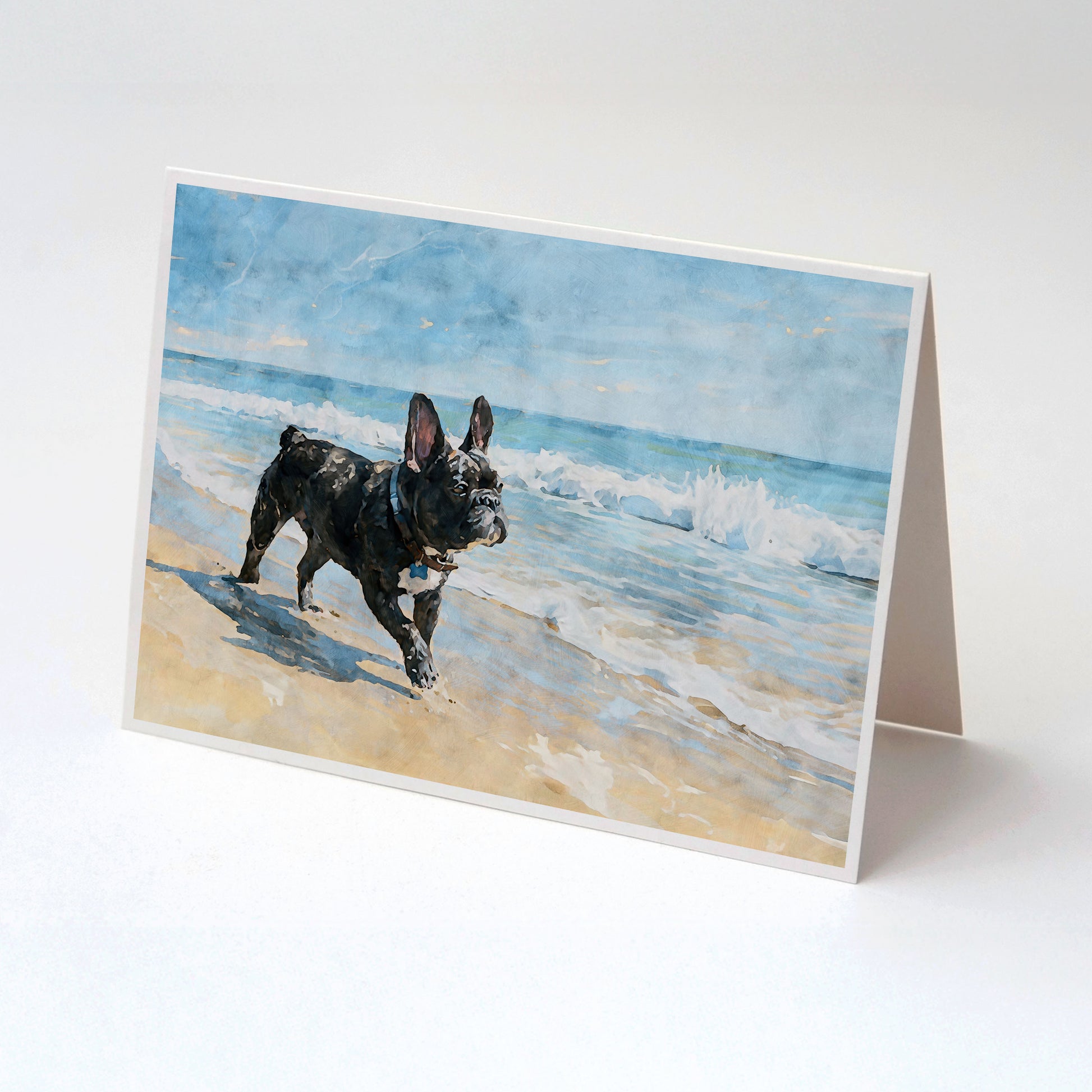Tented folded note card featuring a brindle French Bulldog standing on a beach with soft blue waves.