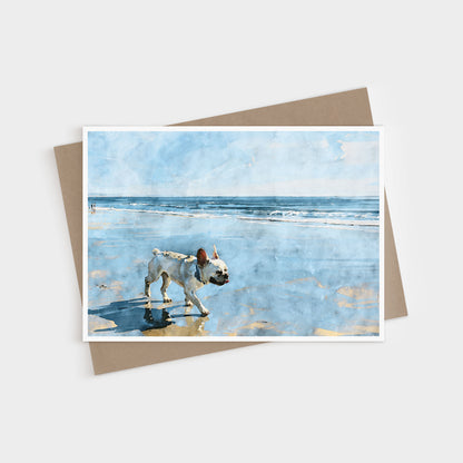 Cream French Bulldog beach note card displayed with a kraft envelope and soft blue coastal watercolor artwork.