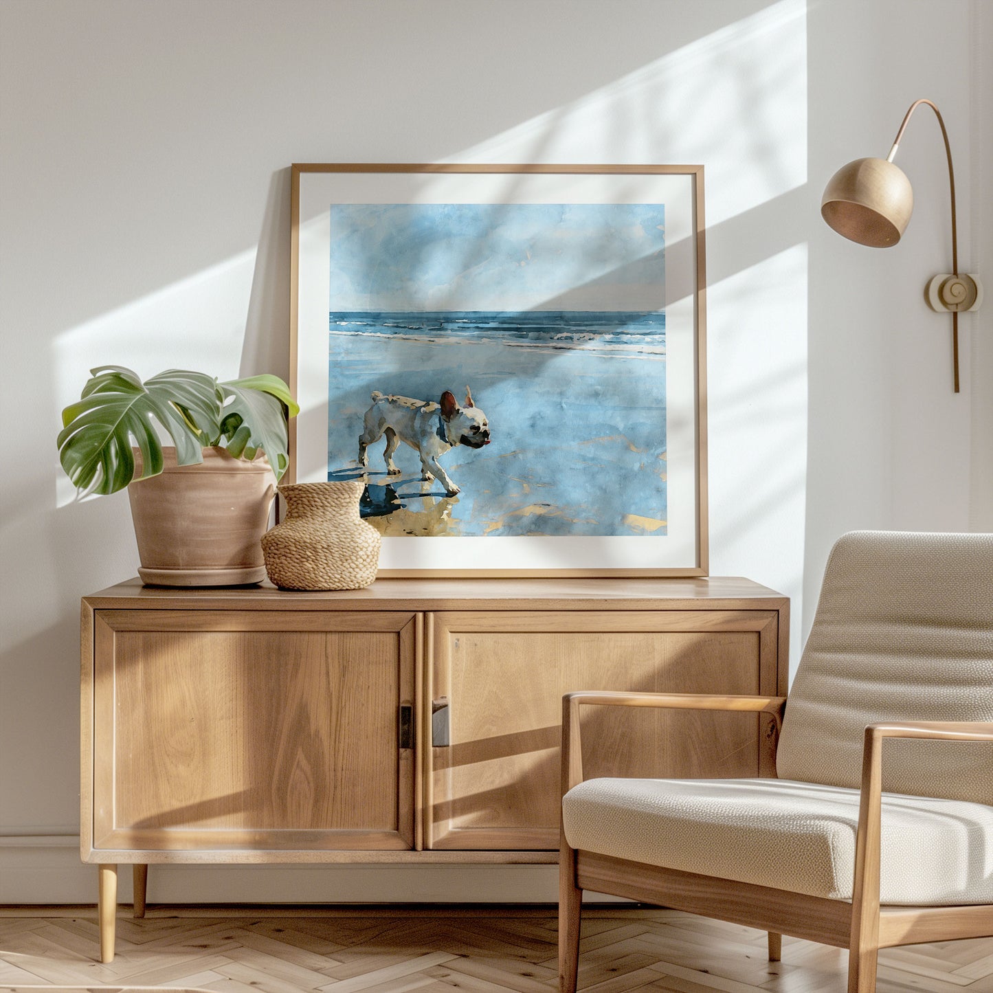 Square framed watercolor print of a cream French Bulldog on a beach shown in a styled interior.