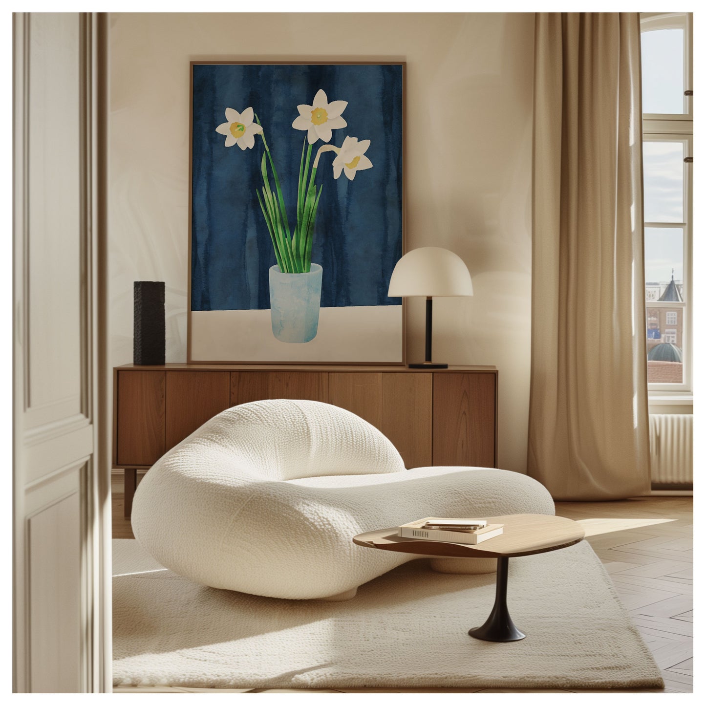 A stylish interior featuring a framed artwork of three white daffodils in a light blue vase on a white surface against a dark blue background, displayed above a wooden credenza. A modern beige lounge chair and coffee table occupy the foreground.