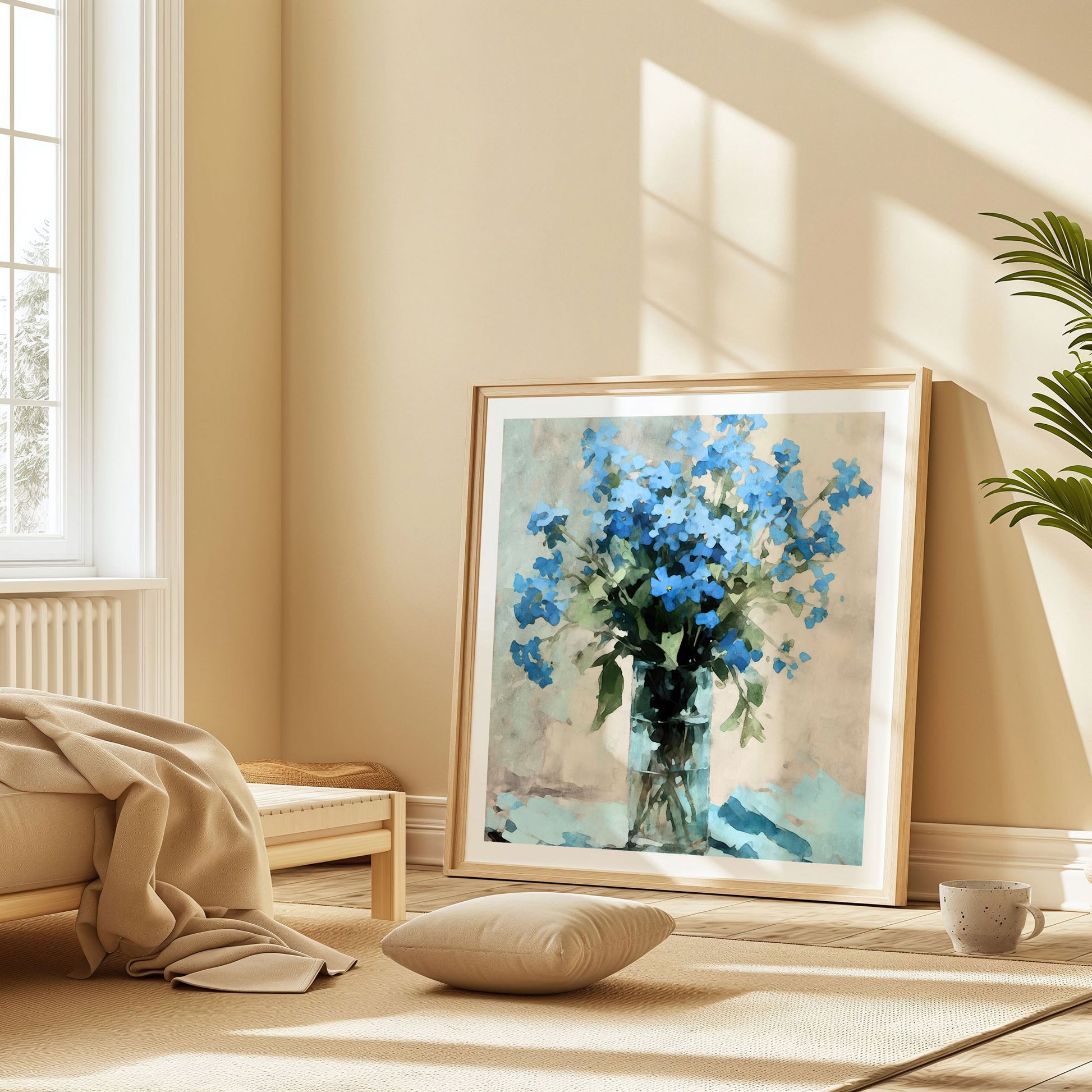 Sunlit room featuring a large framed watercolor painting of vibrant blue forget-me-nots in a clear glass vase, leaning against a wall beside a window, with a cushion and a cup on a rug nearby.