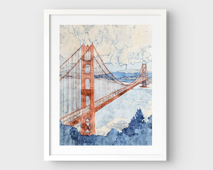 Watercolor-style painting of the Golden Gate Bridge, viewed at an angle with one tower in the foreground and the second in the distance. The bridge is rendered in soft rust red tones, stretching across a pale blue bay with hills and buildings in the background, and a cloudy sky above. Framed in white with a white border.