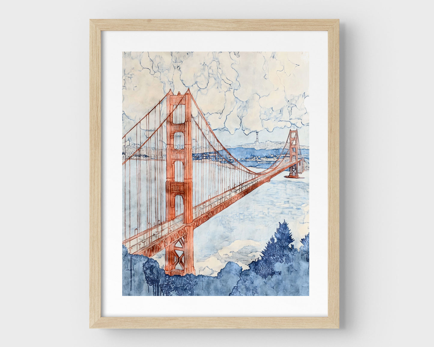 Watercolor-style painting of the Golden Gate Bridge, viewed at an angle with one tower in the foreground and the second in the distance. The bridge is rendered in soft rust red tones, stretching across a pale blue bay with hills and buildings in the background, and a cloudy sky above. Framed in natural wood with a white border.