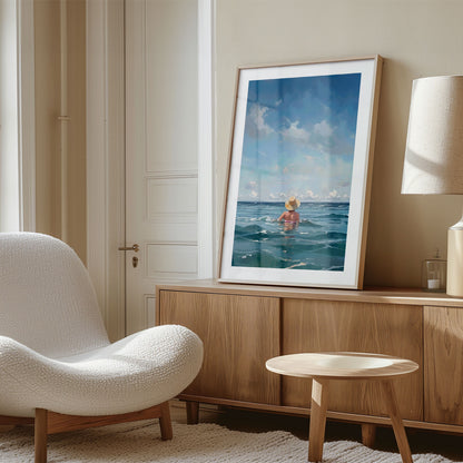 Framed painting of a person in the ocean displayed on a wooden sideboard next to a white textured chair in a well-lit room.