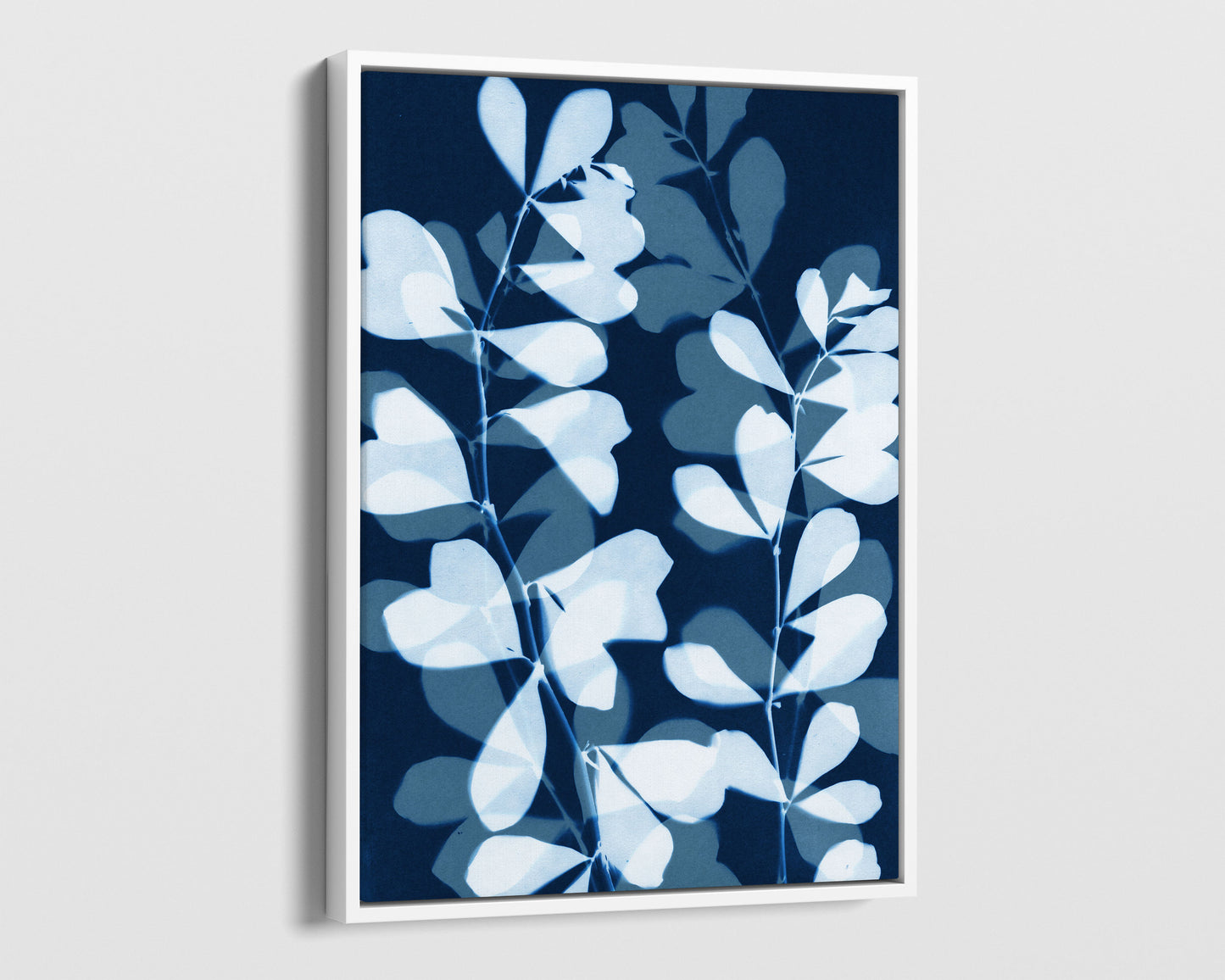 White framed canvas print featuring overlapping cyanotype-style botanical leaves in soft blue and white against a deep navy background, creating a layered, translucent effect.