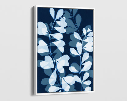White framed canvas print featuring overlapping cyanotype-style botanical leaves in soft blue and white against a deep navy background, creating a layered, translucent effect.