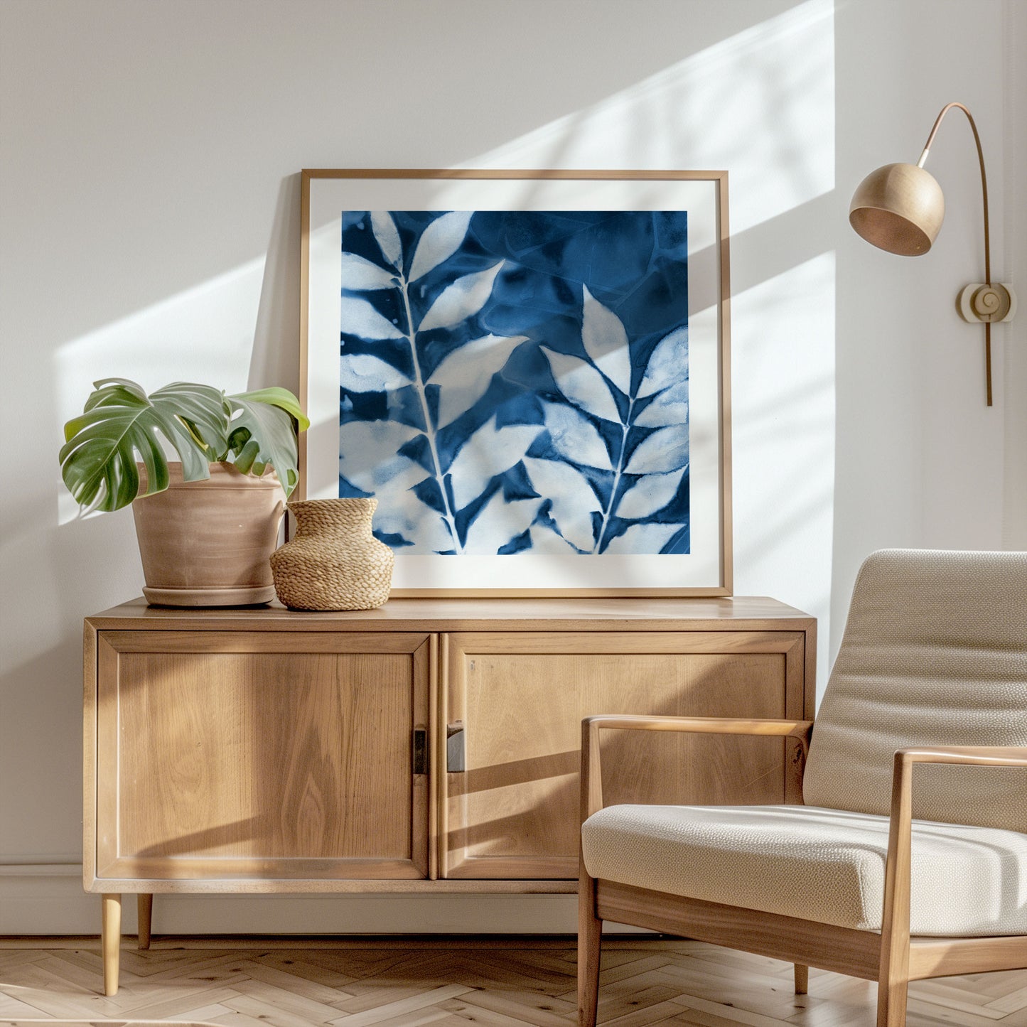 Framed cyanotype print of leafy branches in deep blue and white, displayed on a wooden sideboard with natural decor in a sunlit room.