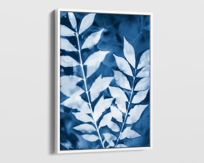 White framed cyanotype print of two leafy branches in deep blue and white, highlighting organic textures and intricate vein details.