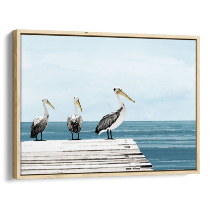 Natural wood framed canvas print featuring three pelicans standing on a weathered white dock above calm blue ocean water, under a soft, cloudy sky.