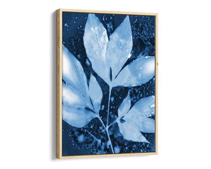 Natural wood framed canvas of a cyanotype-inspired peony leaf cluster, rendered in soft pale blue against a rich indigo background with organic speckled textures and fluid, cloud-like shapes.