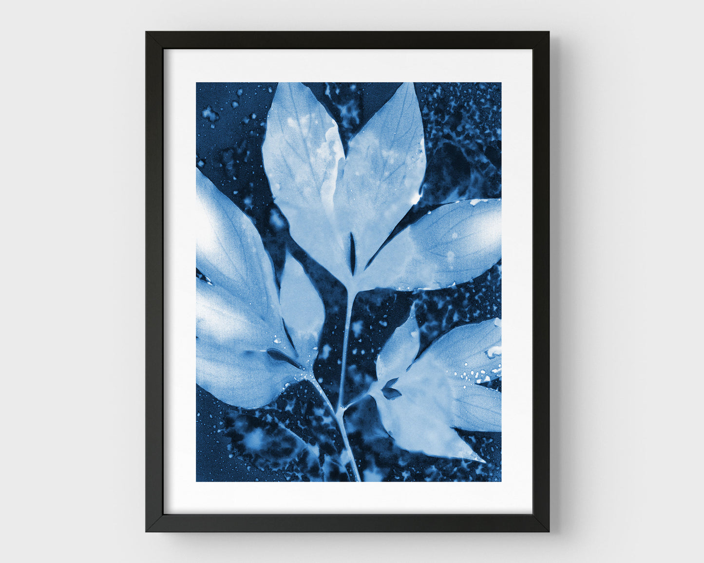 Framed cyanotype print of peony leaves in rich indigo and soft blue tones, featuring delicate leaf silhouettes and organic speckling, set against a clean white background with a black frame.