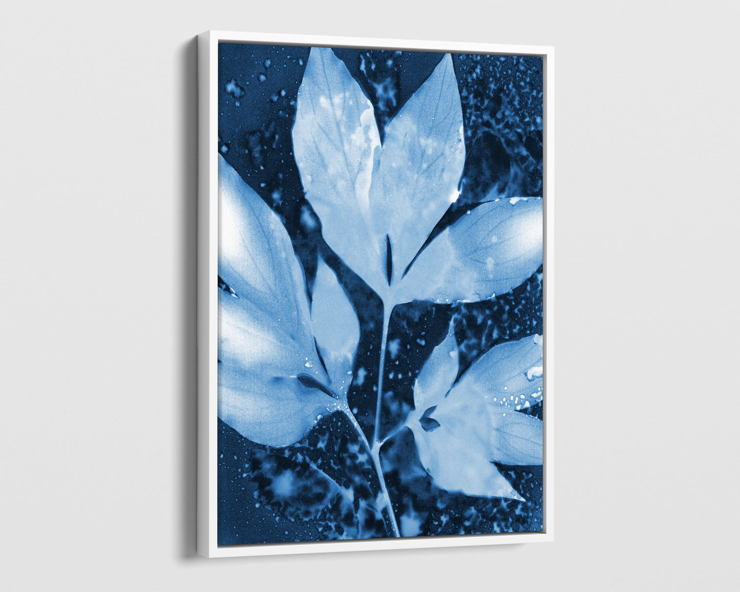 White framed canvas of a cyanotype-inspired peony leaf cluster, rendered in soft pale blue against a rich indigo background with organic speckled textures and fluid, cloud-like shapes.