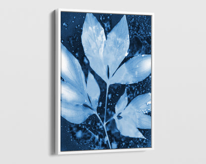 White framed canvas of a cyanotype-inspired peony leaf cluster, rendered in soft pale blue against a rich indigo background with organic speckled textures and fluid, cloud-like shapes.