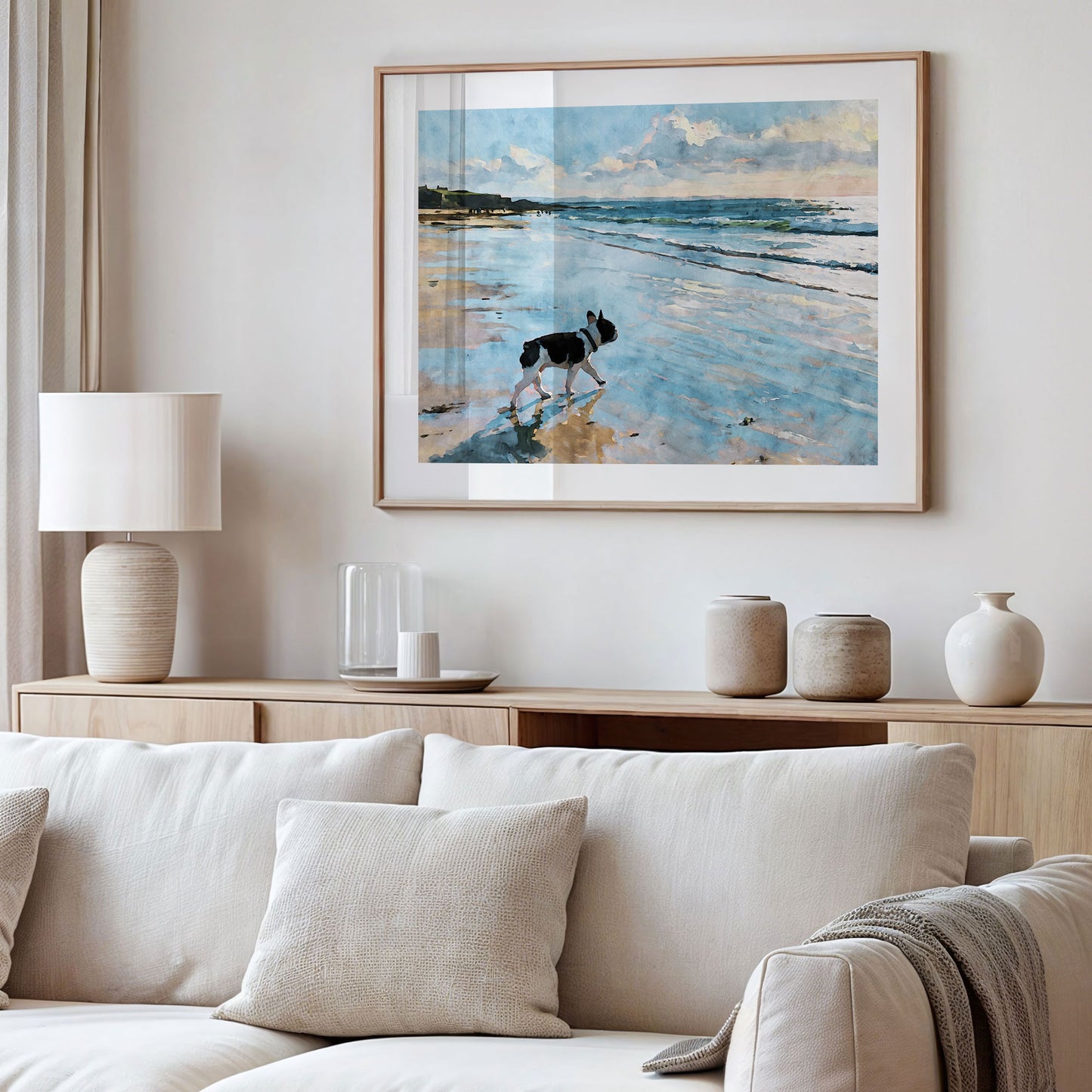 Framed pied French Bulldog beach watercolor art displayed in a styled interior with soft blue and sandy neutral tones.