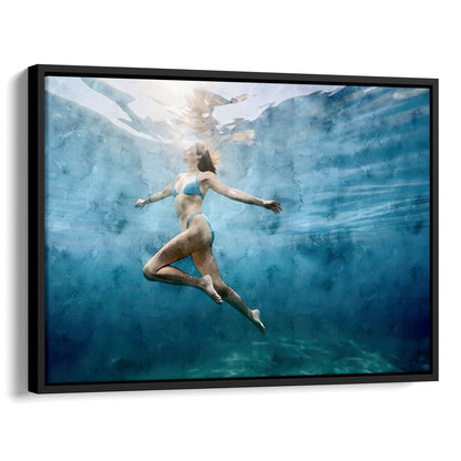 Watercolor painting of an underwater view of a woman in a blue swimsuit swimming upward, surrounded by blue-green water with light filtering from above. Artwork printed on gallery wrap canvas in black floater frame.