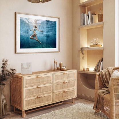 Interior with light wood dresser, wicker chair, and built-in shelves, featuring a framed underwater art print on the wall