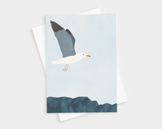 Minimalist illustration of a seagull in flight above dark blue coastal rocks, set against a pale blue sky, featured on a greeting card with a white envelope behind it.
