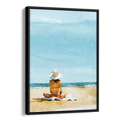 Black framed canvas print featuring a person sitting on a towel at a beach, wearing a wide-brimmed hat and a swimsuit, with a clear blue sky and ocean.