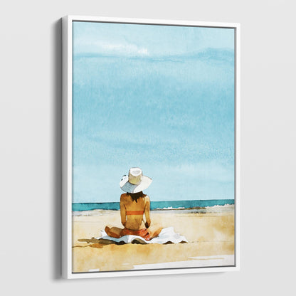 White framed canvas print featuring a person sitting on a towel at a beach, wearing a wide-brimmed hat and a swimsuit, with a clear blue sky and ocean.