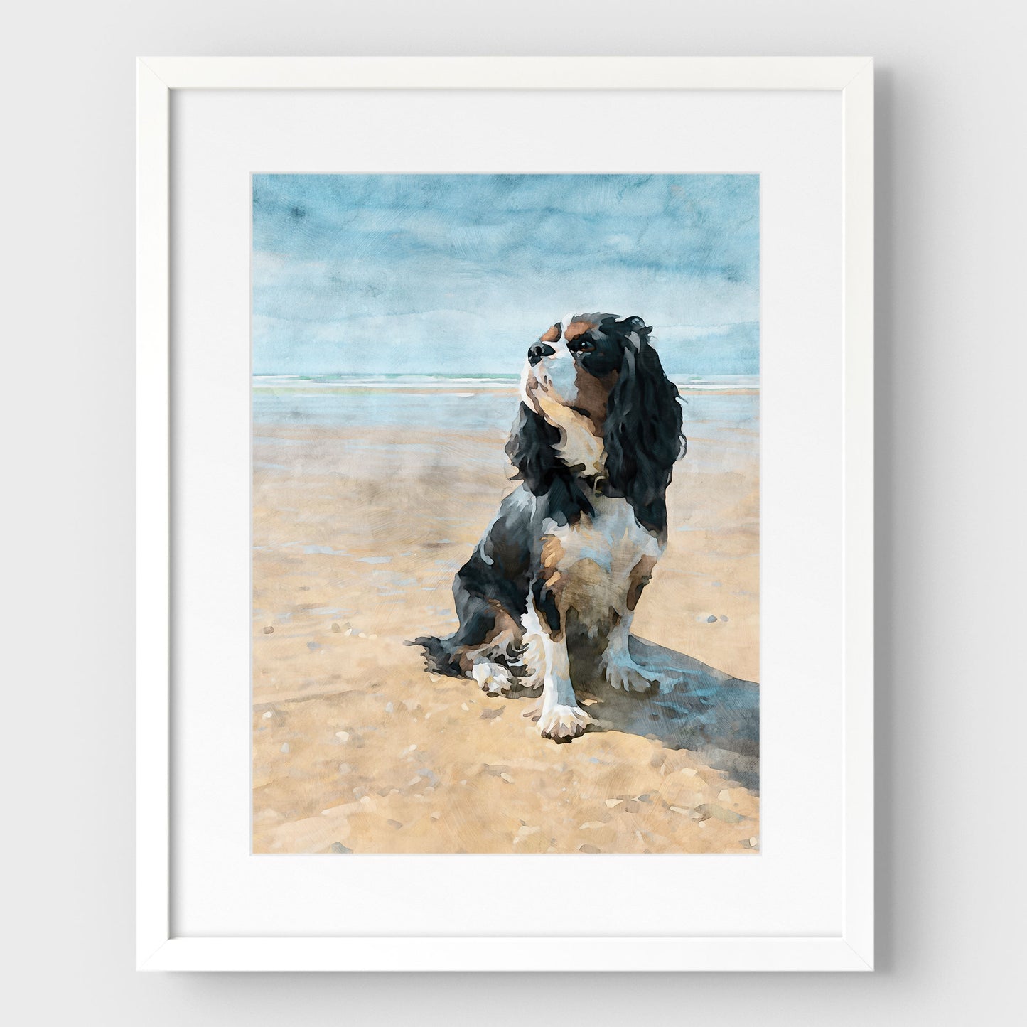 White framed artwork with a white mat of a tricolor King Charles spaniel on a beach with a watercolor background