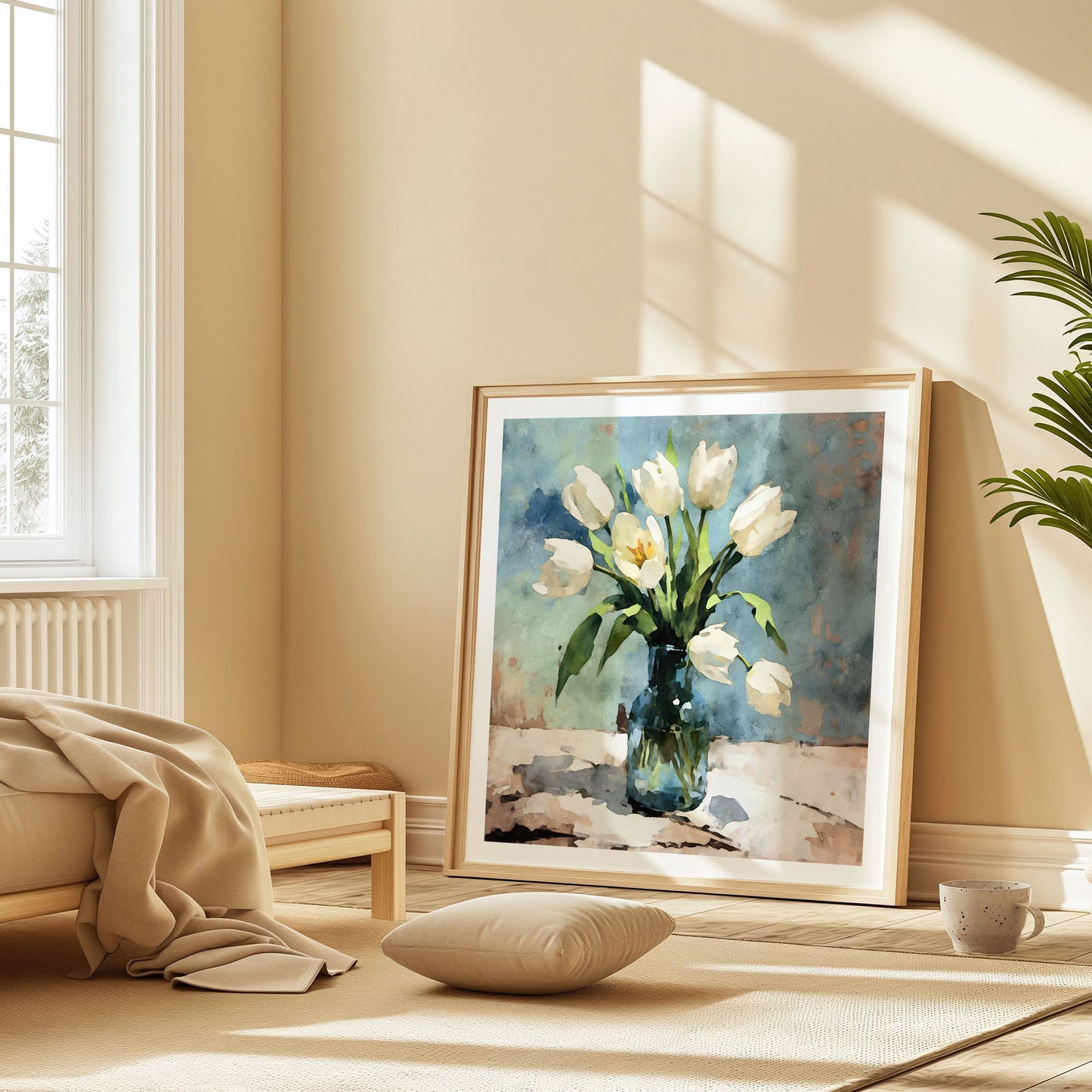 Sunlit room featuring a large framed watercolor painting of white tulips in a blue vase, leaning against a wall beside a window, with a cushion and a cup on a rug nearby.