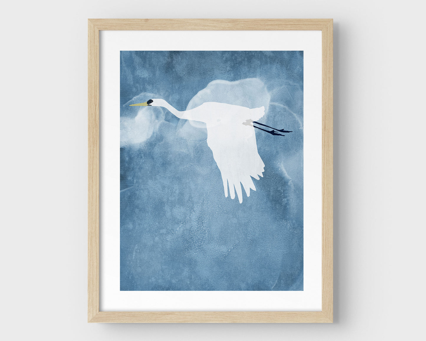 Minimalist natural wood framed print of a white heron flying with wings lowered against a textured blue sky with soft, cloud-like forms in the background.
